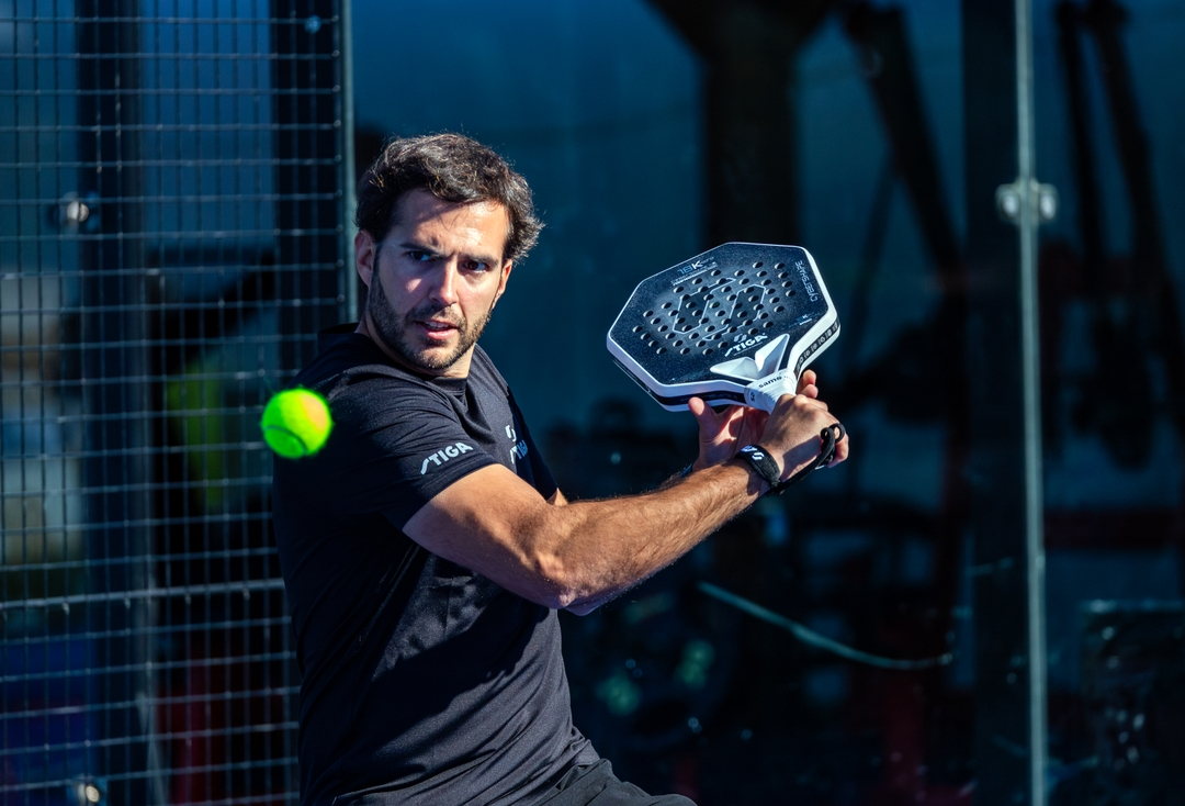 A player striking a STIGA Cybershape racket on a floodlit padel court